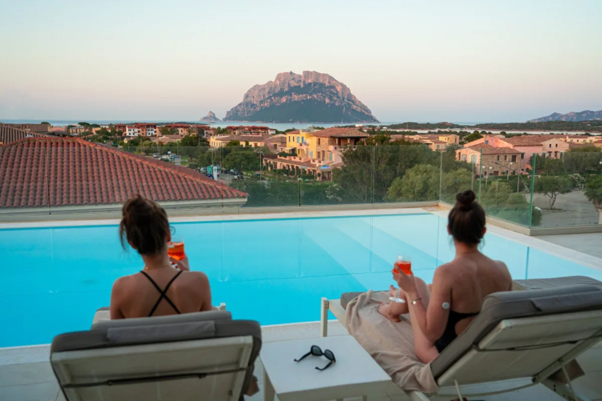 Due donne rilassate sui lettini a bordo piscina con vista Tavolara al tramonto