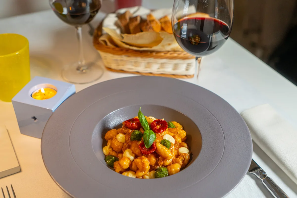 Gnocchi con pomodoro, basilico e pesto serviti in piatto grigio con vino rosso