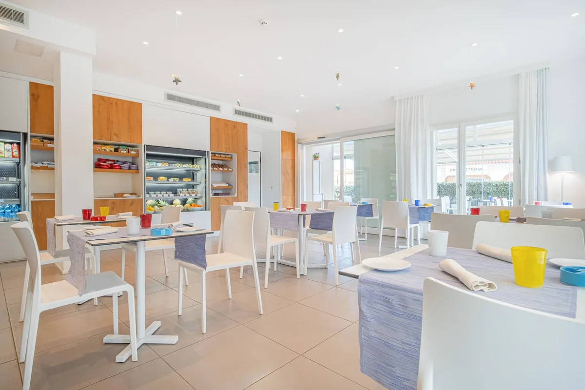 Sala colazione luminosa con tavoli bianchi e buffet self-service