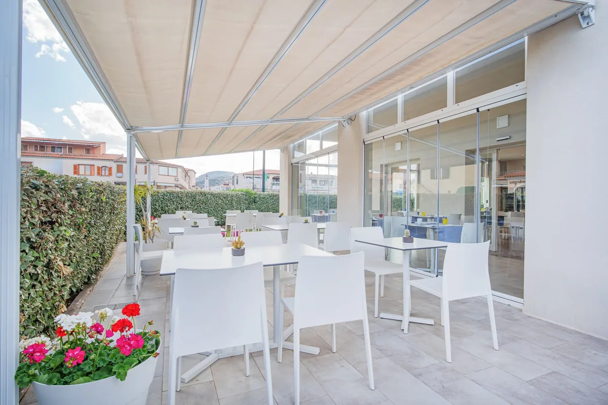 Terrazza esterna del ristorante con tavoli bianchi e tenda parasole