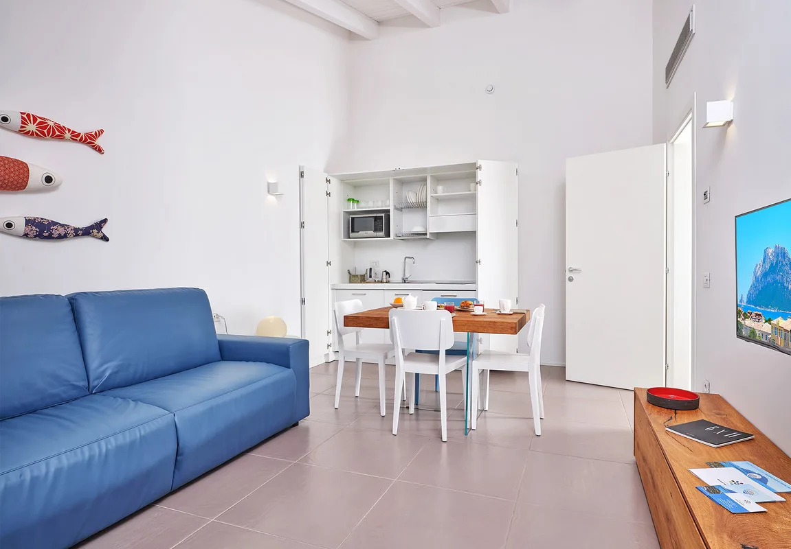 Soggiorno luminoso dell'appartamento con divano blu, angolo cottura e tavolo in legno