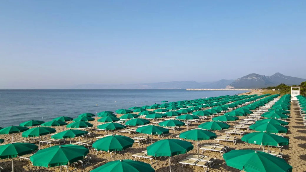 File di ombrelloni verdi sulla spiaggia con vista mare e montagne