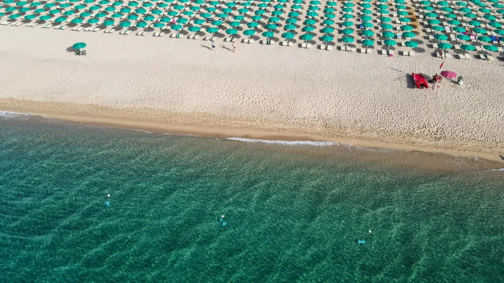 Vista aerea della spiaggia con ombrelloni verdi e mare trasparente