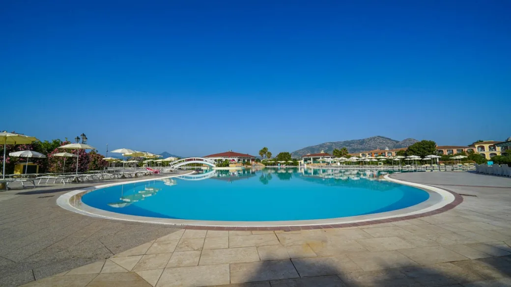 Piscina del resort con ponte e ombrelloni sotto il cielo azzurro