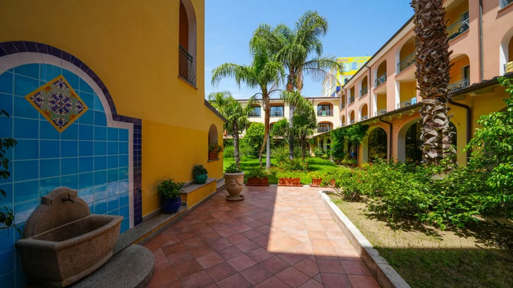 Cortile interno con fontana a maioliche, palme e giardino