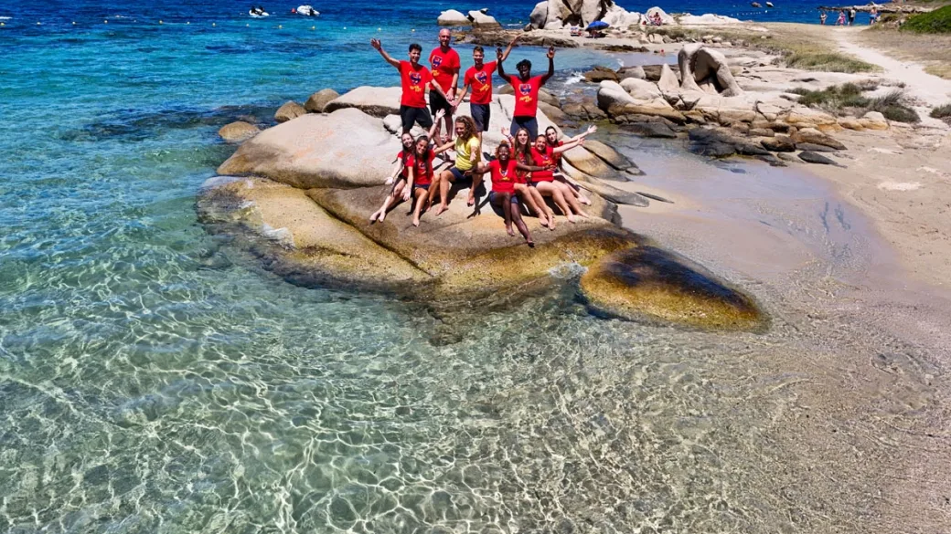 Gruppo di animatori in maglietta rossa posa su una roccia in riva al mare