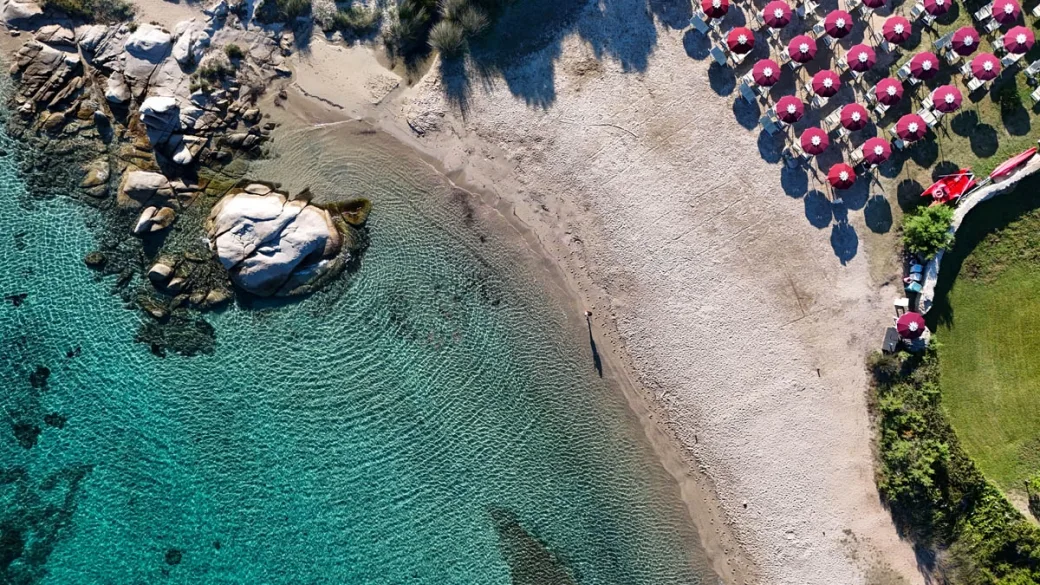 Vista dall'alto della spiaggia con ombrelloni rossi e mare cristallino