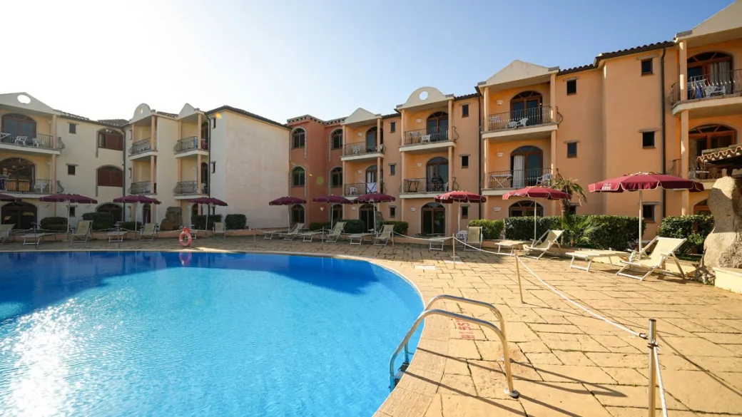 Piscina del residence con edifici colorati, ombrelloni e lettini