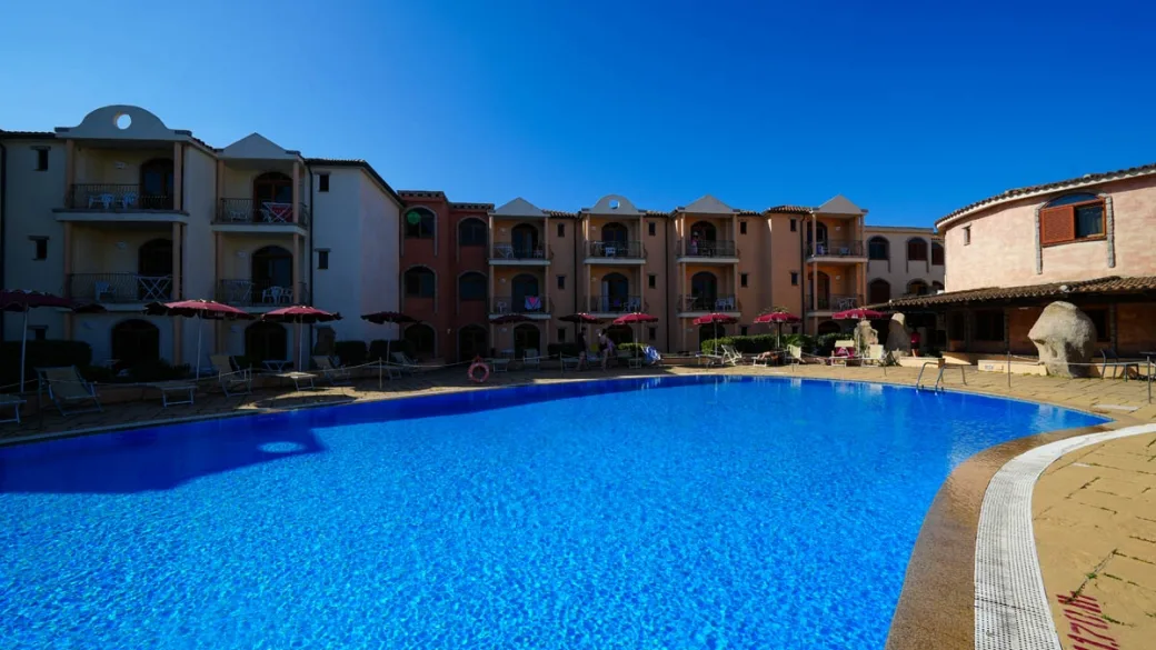 Ampia piscina del residence circondata da edifici e ombrelloni rossi