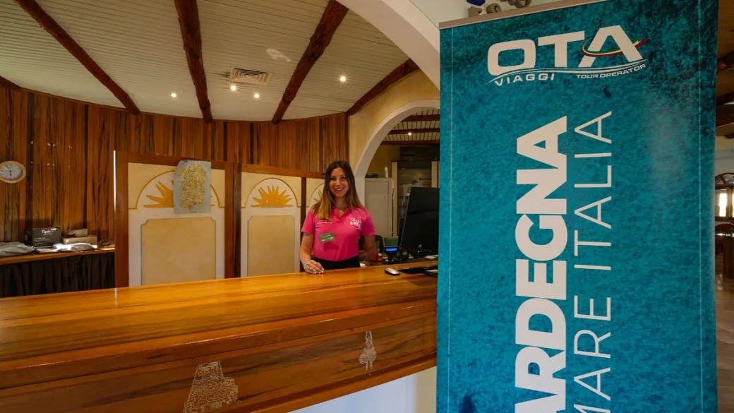 Reception con receptionist e roll-up del tour operator Sardegna