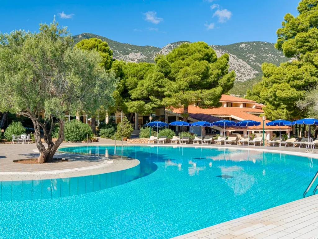 Piscina con ulivo centrale e ombrelloni blu tra le montagne