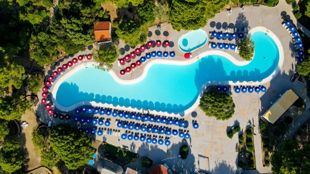 Vista aerea della grande piscina sinuosa con lettini e ombrelloni colorati