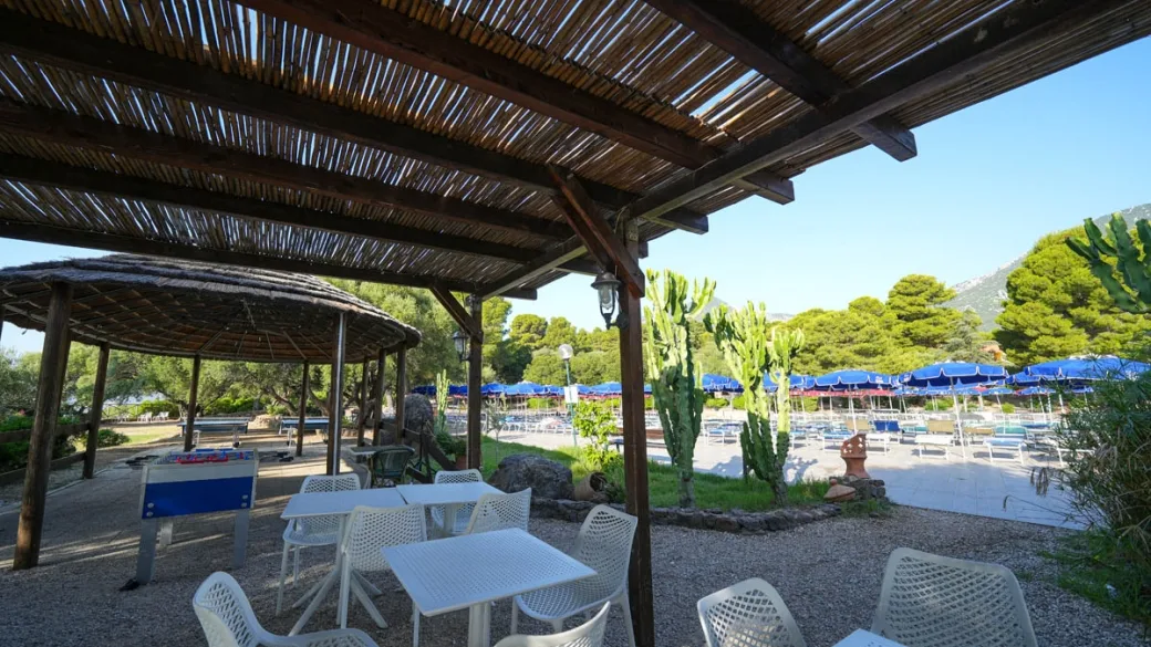 Area relax con pergolato in legno e tavolini bianchi vicino alla piscina