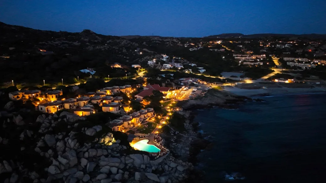 Vista notturna del villaggio illuminato con piscina e cottage lungo la costa