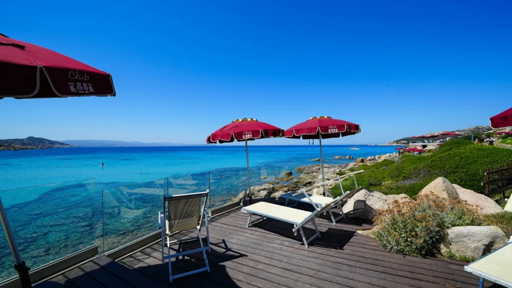 Terrazza solarium con lettini e ombrelloni rossi affacciata sul mare cristallino