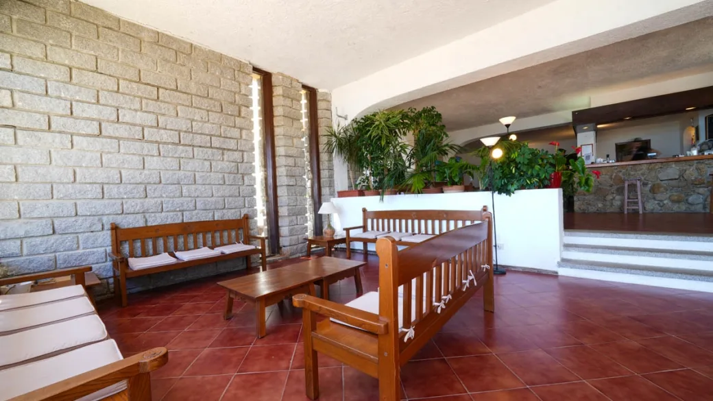 Area lounge interna con divani in legno, piante e bancone reception