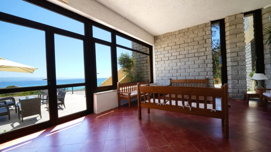 Veranda interna con grandi vetrate, panche in legno e vista sul mare