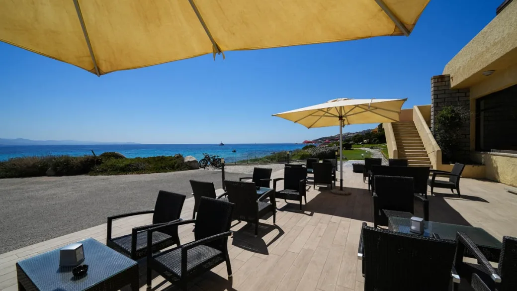 Terrazza bar con tavoli, poltrone e ombrelloni gialli affacciata sul mare
