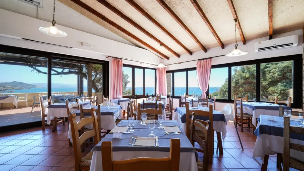 Sala ristorante interna con travi a vista, tavoli apparecchiati e vista mare
