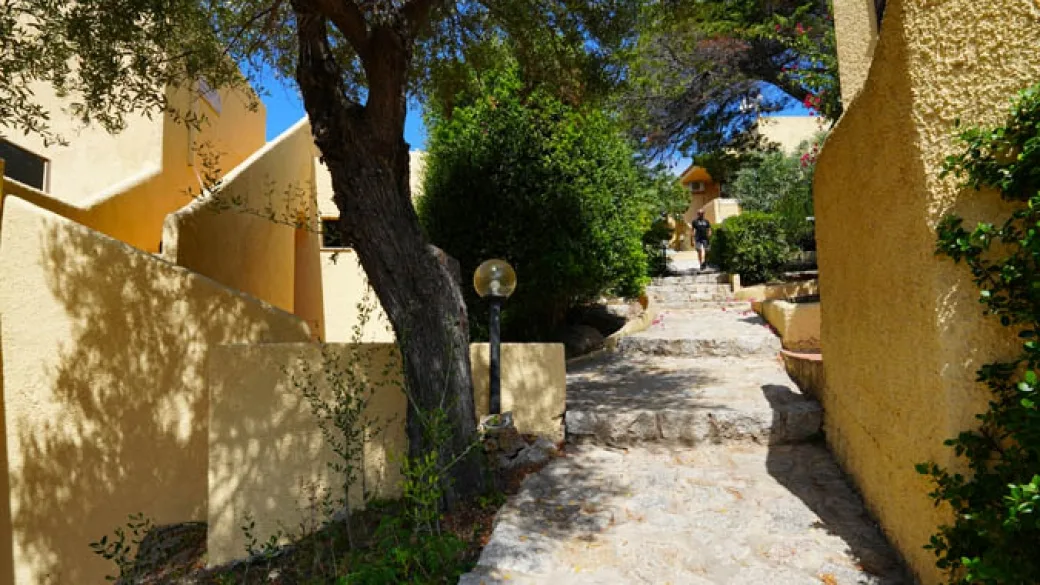 Vialetto in pietra tra cottage gialli e vegetazione mediterranea