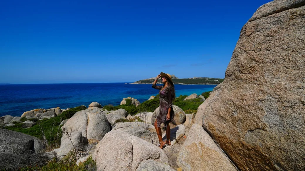 Donna con cappello tra le rocce di granito affacciata sul mare blu
