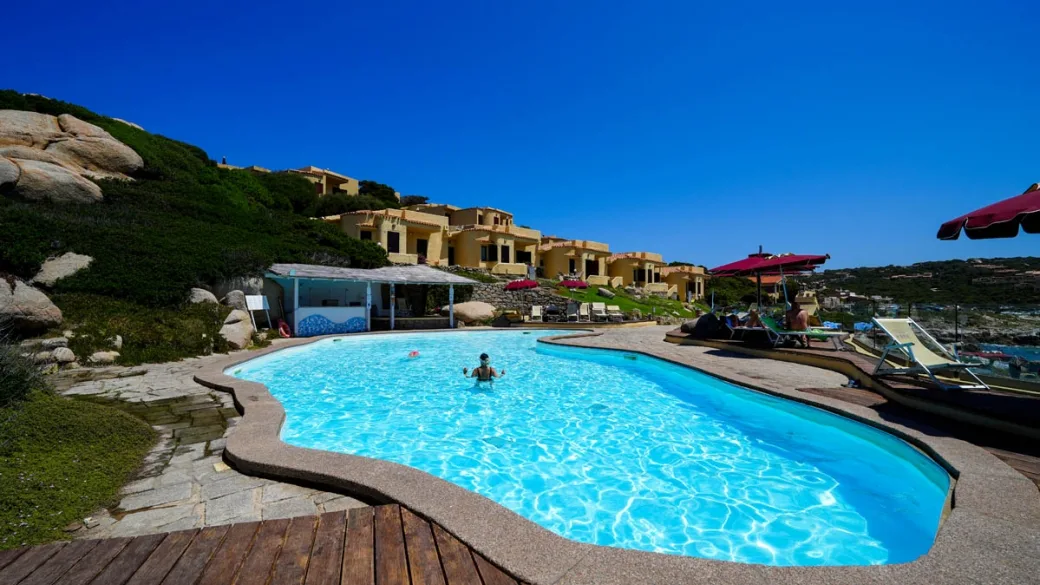 Piscina esterna con vista sui cottage e ombrelloni rossi