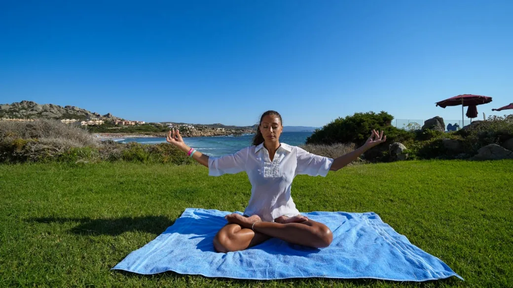 Donna in meditazione yoga sul prato verde affacciato sul mare