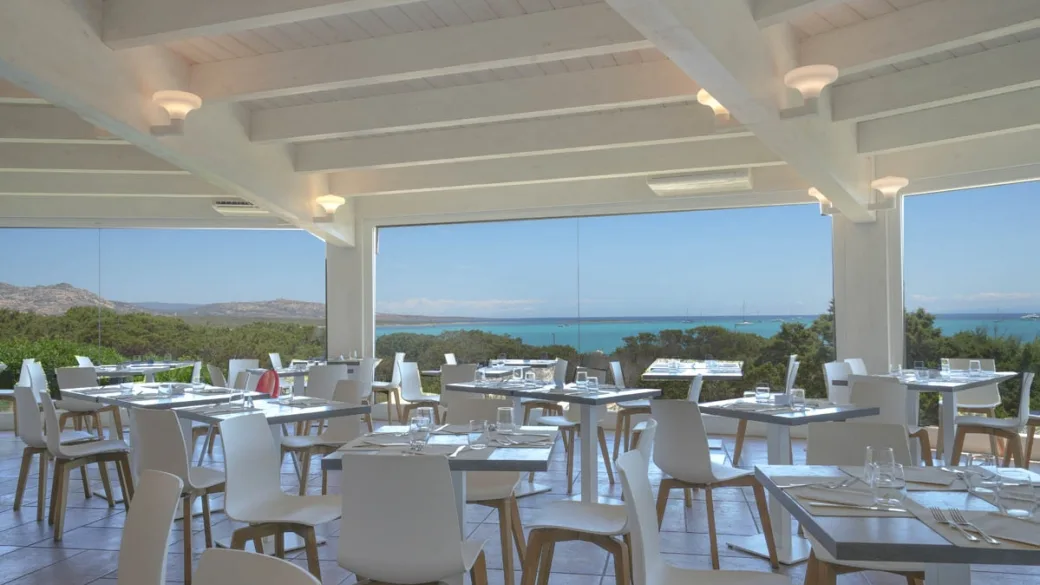 Sala ristorante luminosa con tavoli e grandi vetrate affacciate sul mare