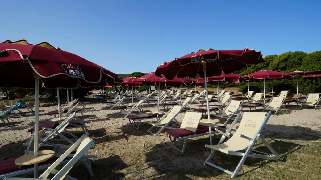File di lettini e ombrelloni rossi Club Esse sulla spiaggia sabbiosa