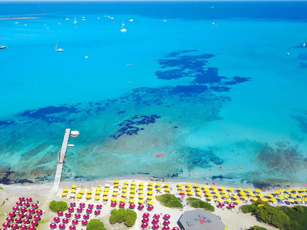 Spiaggia con ombrelloni gialli e rossi e mare azzurro con barche a vela