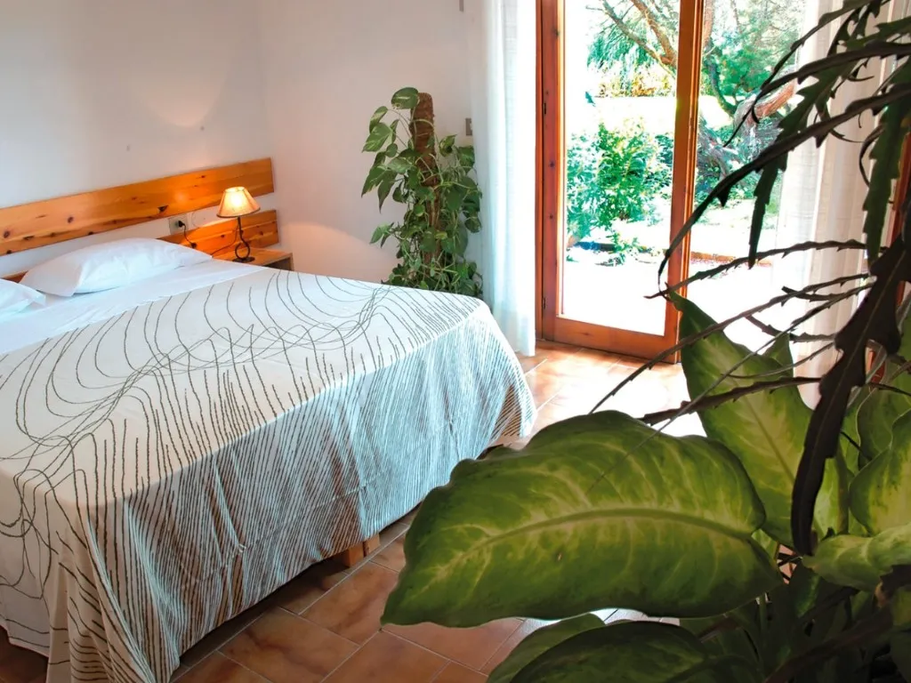 Camera accogliente con letto, piante verdi e uscita sul giardino