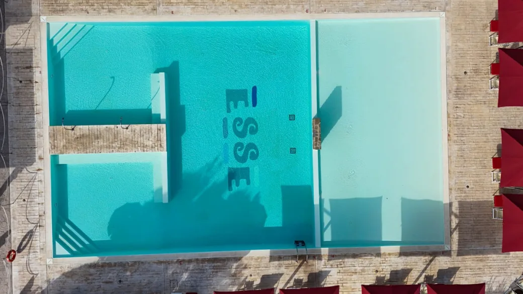 Vista dall'alto della piscina con scritta Esse sul fondo e ombrelloni rossi