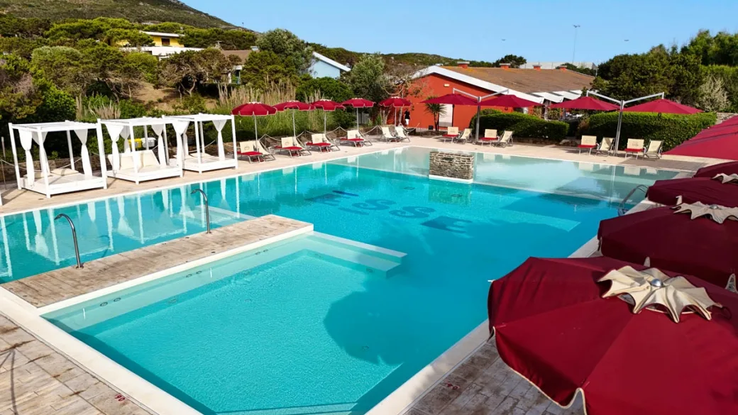Piscina con gazebo bianchi e ombrelloni rossi circondata da vegetazione