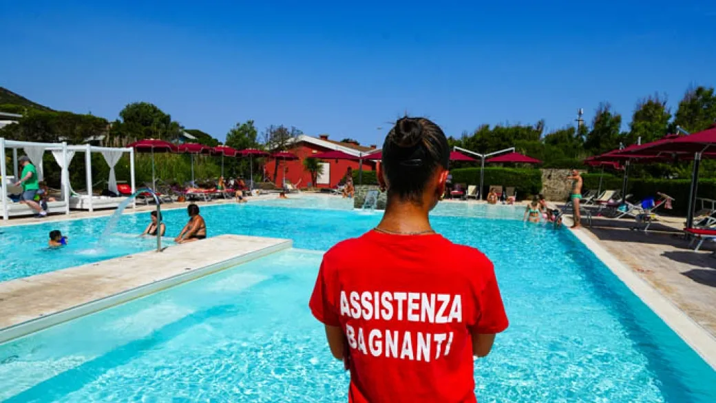 Assistente bagnanti accanto alla piscina con ospiti in acqua