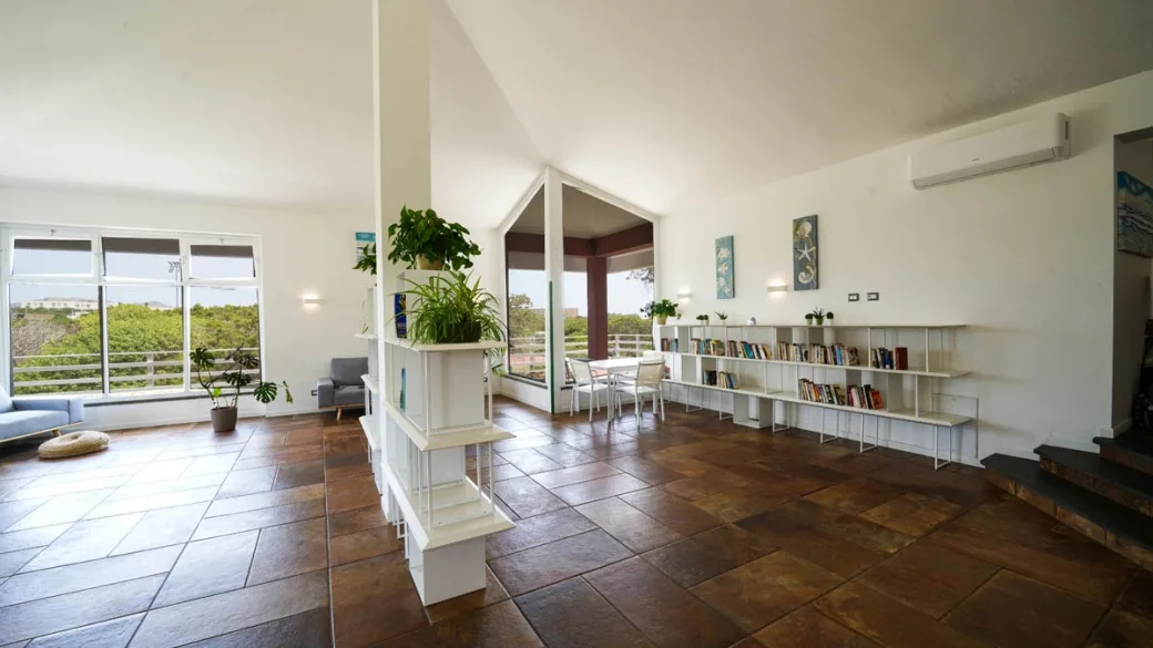 Sala comune luminosa con libreria, divano e grandi vetrate sul verde