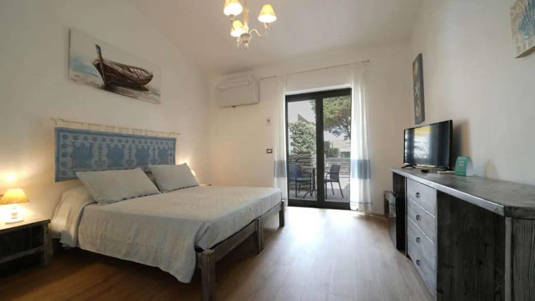 Camera matrimoniale con TV, arredi in legno e porta-finestra sul terrazzo