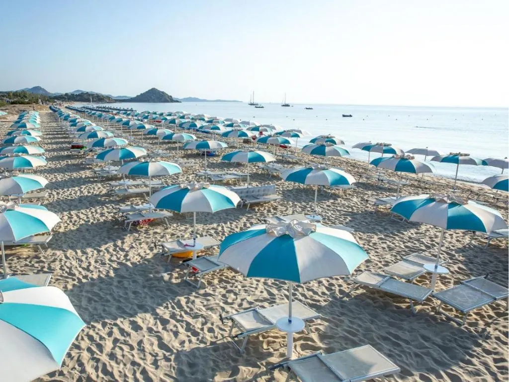 File di ombrelloni azzurri e bianchi con lettini sulla spiaggia di sabbia affacciata sul mare