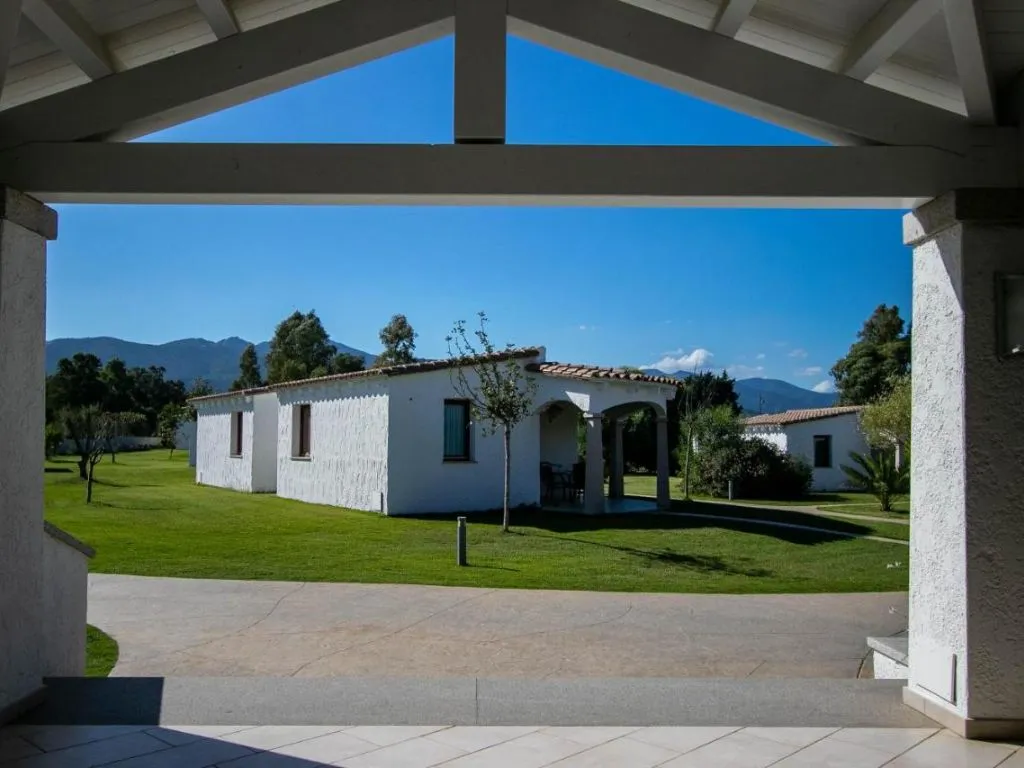 Vista da un portico verso una villa bianca con prato verde e montagne sullo sfondo