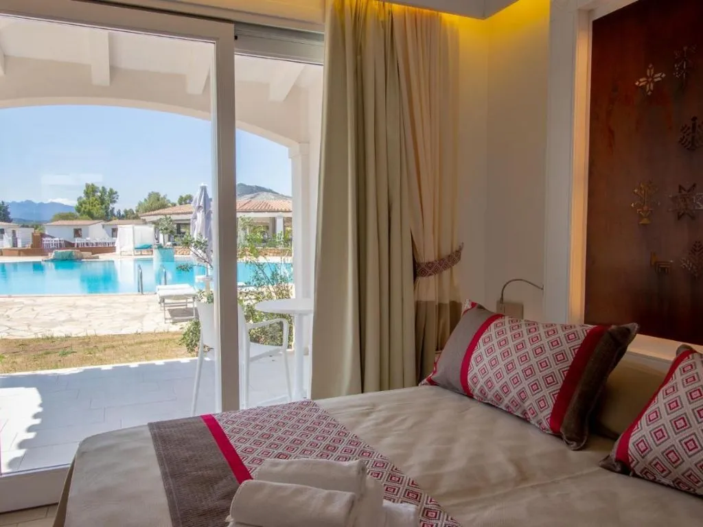 Camera con letto e porta-finestra affacciata sulla piscina e le ville del resort