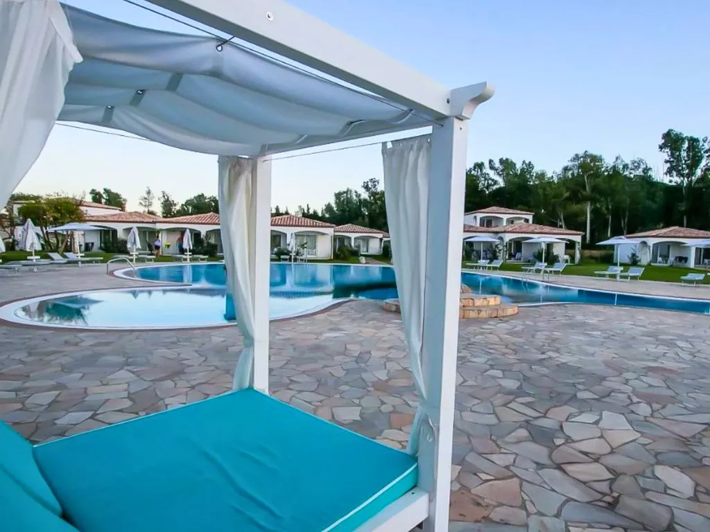 Letto baldacchino con materasso turchese accanto alla piscina e ville sullo sfondo