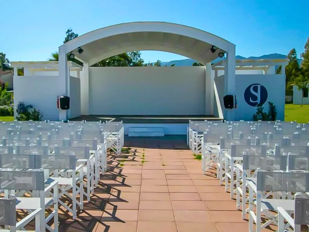 Palco esterno bianco per eventi con file di sedie bianche e montagne sullo sfondo