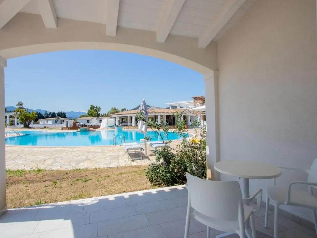 Vista dal portico di una camera verso la piscina con tavolino e sedie bianche