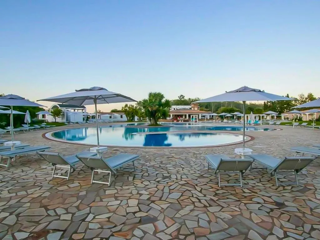 Ampia piscina rotonda con lettini e ombrelloni bianchi al tramonto