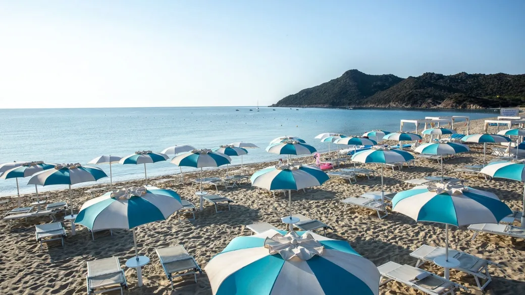 Spiaggia con ombrelloni bianchi e azzurri e lettini davanti al mare con promontorio roccioso