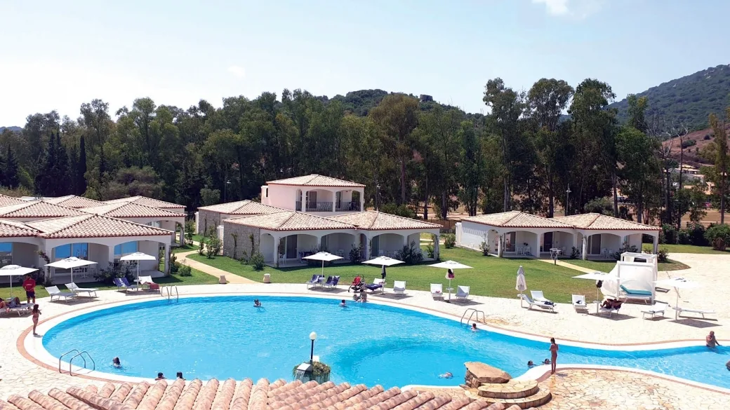 Piscina con bagnanti circondata da ville bianche con tetti in tegole e colline boscose