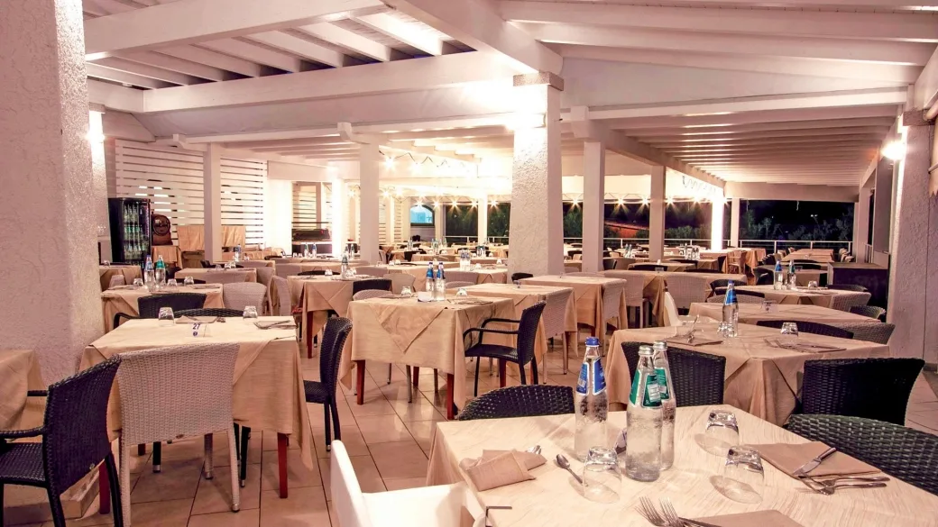 Sala ristorante con tavoli apparecchiati, tovaglie chiare e illuminazione serale