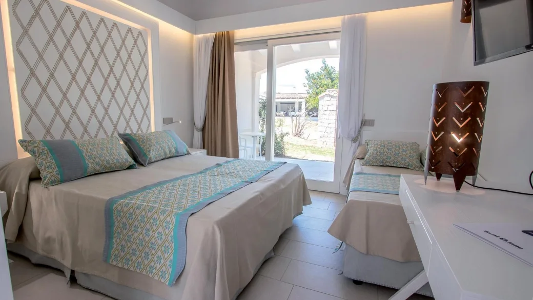 Camera con letto matrimoniale e letto singolo, testiera decorata e porta-finestra sul giardino