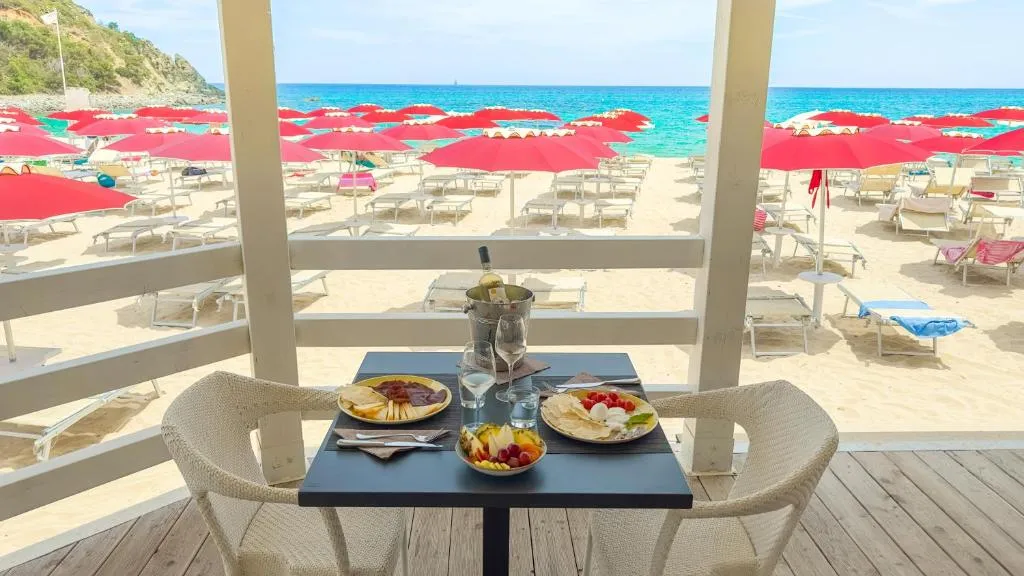 Tavolo con aperitivo affacciato sulla spiaggia con ombrelloni rossi e mare