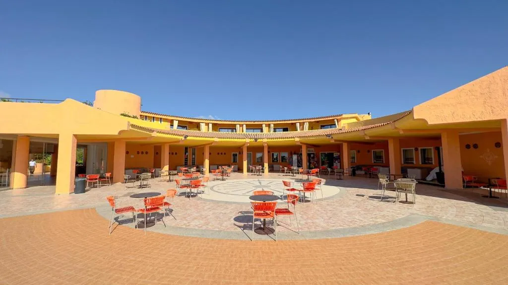 Cortile interno del resort con tavoli, sedie arancioni e portici