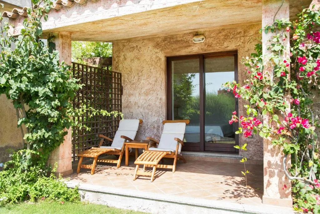 Veranda di villetta con lettini in legno tra fiori e vegetazione